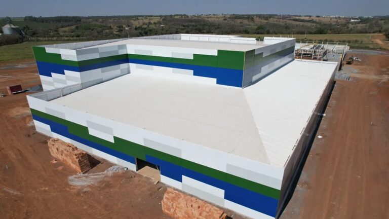 Prédio industrial de grande porte com faixas verde e azul em construção em área rural visto de cima