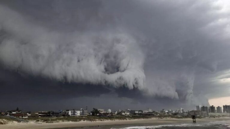 Nuvem de tempestade avança sobre área urbana no litoral com céu escuro e mar em primeiro plano durante evento climático extremo
