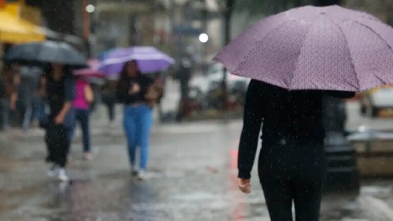 Pedestres caminham com guarda-chuvas em rua sob chuva intensa em imagem sobre previsão do tempo e temporais na cidade