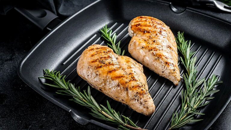 Peitos de frango grelhados em frigideira com ramos de alecrim em imagem sobre preparo e consumo de carne de frango