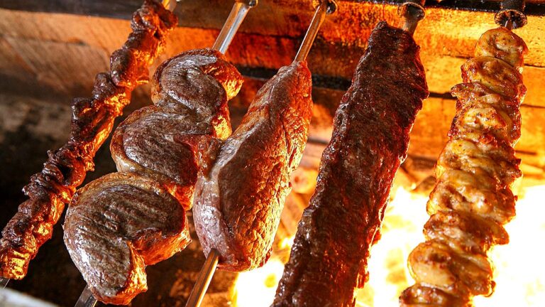 Espetos de carne bovina e frango assando em churrasqueira com fogo intenso ao fundo estilo churrasco brasileiro