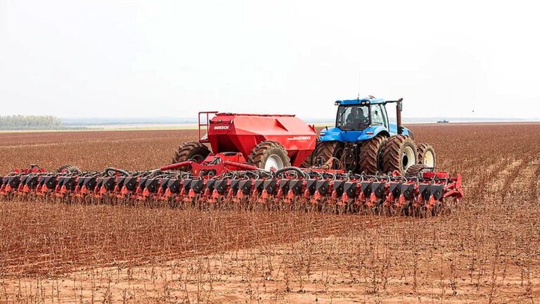Trator agrícola com plantadeira realiza semeadura em grande lavoura de cultivo no campo