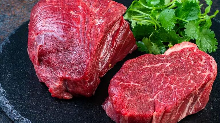 Cortes de carne bovina crua sobre tábua escura com folhas verdes ao fundo