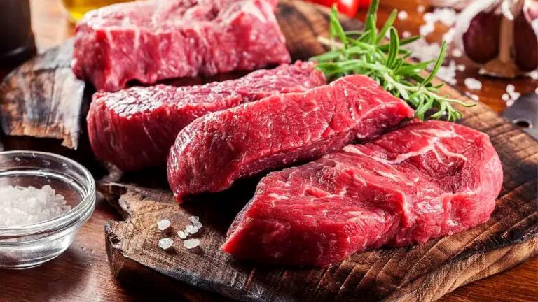 Cortes de carne bovina crua sobre tábua de madeira com sal grosso e ervas frescas