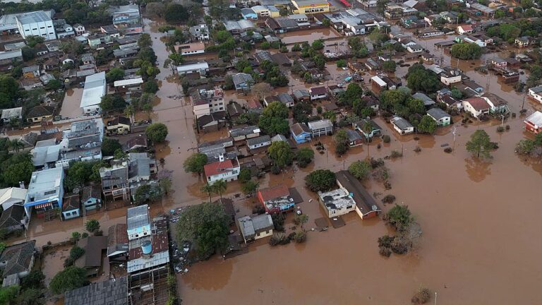 Vista aérea de bairro alagado com ruas e casas inundadas após fortes chuvas e enchente urbana