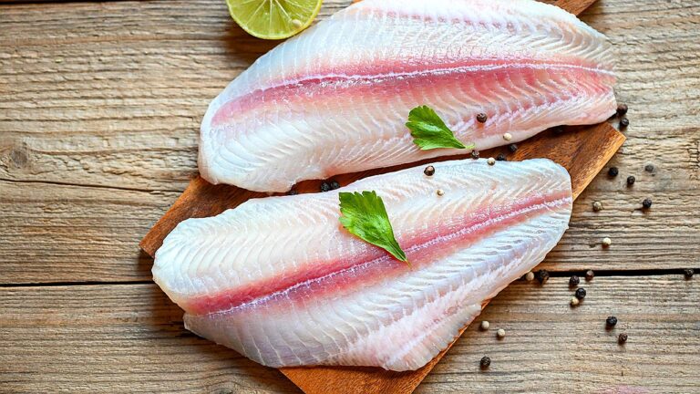 Filés de peixe branco crus sobre tábua de madeira com limão e ervas para preparo culinário