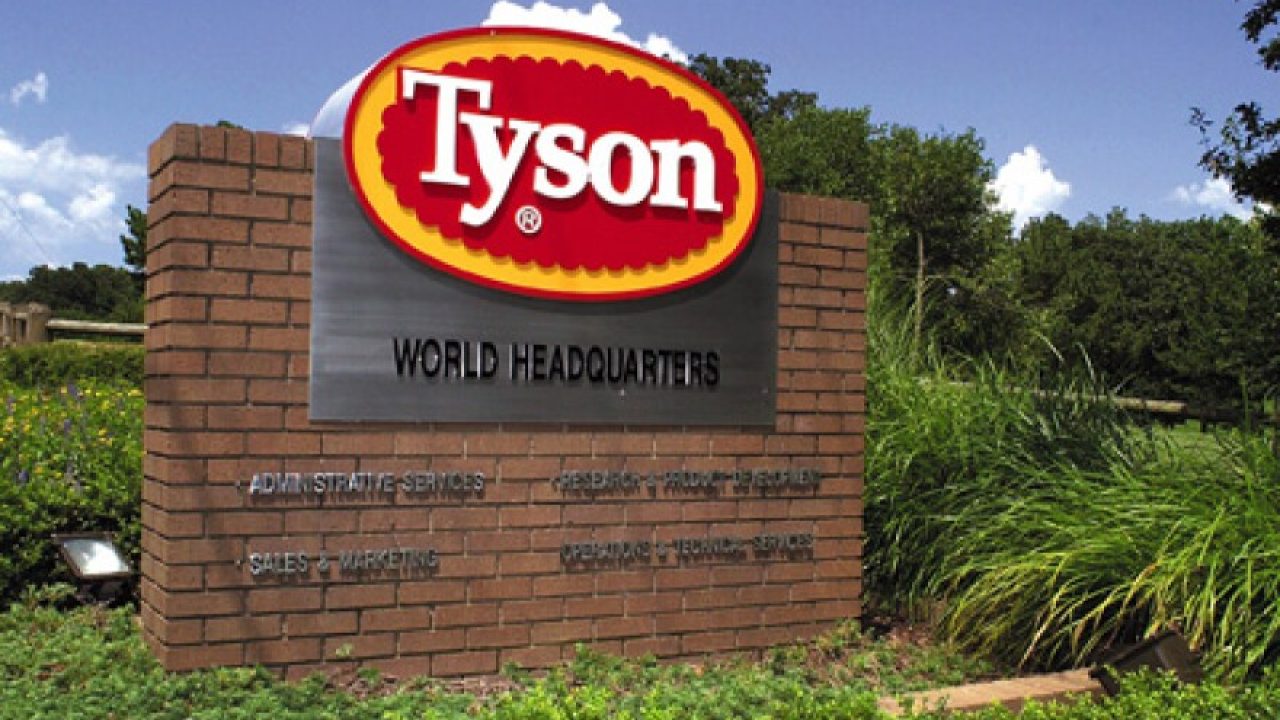 Placa de entrada da sede mundial da Tyson com logotipo vermelho e amarelo em estrutura de tijolos cercada por vegetação